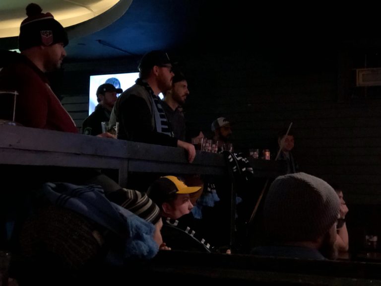 Dark Clouds members sitting at a bar watching the match on a tv offscreen.
