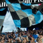 Minnesota United supporters waving flags and cheering in the Supporters Section.