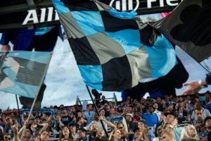 Minnesota United supporters waving flags and cheering in the Supporters Section.