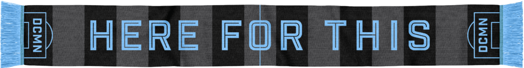 One side of the 2021 scarf, with a powder blue fringe and black and gray stripes. Icons that depict goalie boxes are on either end, giving the scarf the suggestion of a soccer pitch. In powder blue, HERE FOR THIS appears in block letters across the scarf's length.