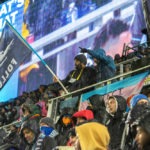 Wonderwall crowd at rain game featuring person waving Dark Clouds Follow flag