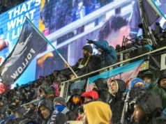 Wonderwall crowd at rain game featuring person waving Dark Clouds Follow flag