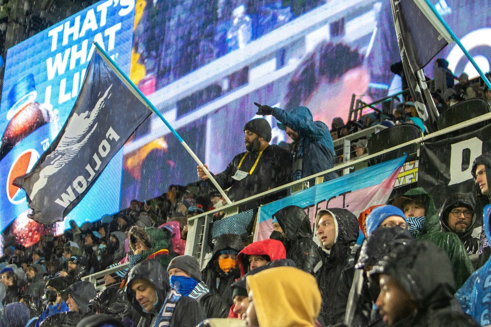 Wonderwall crowd at rain game featuring person waving Dark Clouds Follow flag